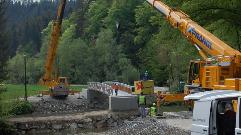 Aluminium-Radwegbrücke schwebt im Tandemhub zwischen zwei Kränen zur Einbaustelle