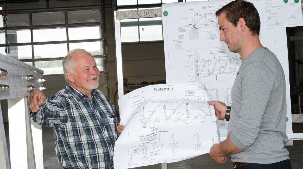 Projektbesprechung von Werner Glück und Andreas Weh mit Brückenplan in der Fertigungshalle.