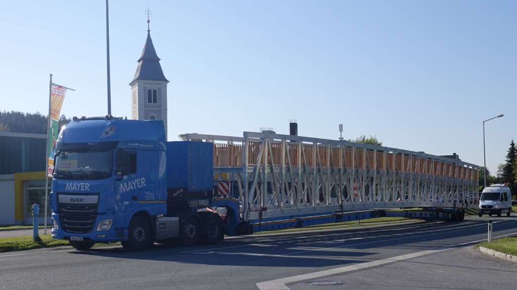 Lange Aluminium-Radwegbrücke auf einem Tieflader beim Transport zur Baustelle im Feistritztal